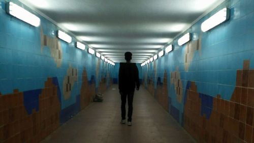 Rear view of man walking in illuminated tunnel