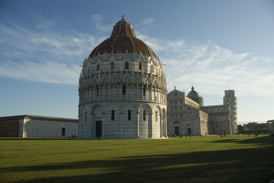 Pisa baptistery on field against sky in city