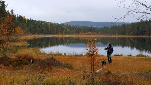 Man walking with dog by lake against sky