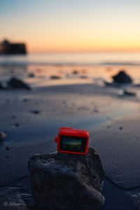 Red rocks at beach against sky during sunset