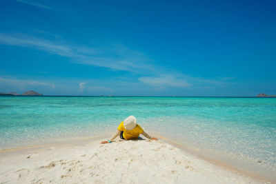 Rear view of woman relaxing at beach against blue sky