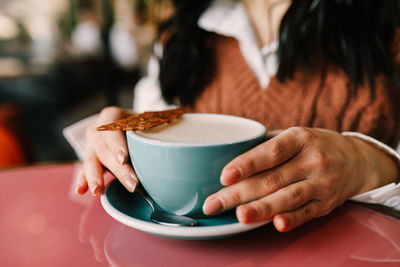 A young smiling woman enjoys a coffee drink while holding a mug while sitting in a cafe