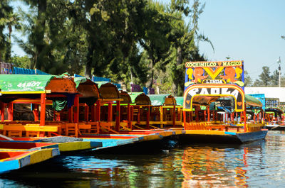 Boats in river by trees against sky