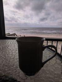 Coffee cup on table by sea against sky