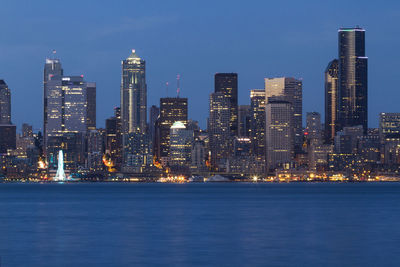 Illuminated buildings by sea against sky