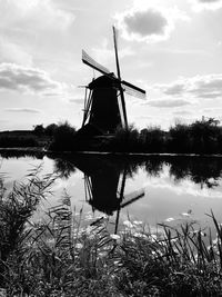 Traditional windmill by lake against sky