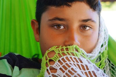 Portrait of teenage boy covering face with knitted curtain