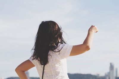 Rear view of woman with arms raised standing against sky