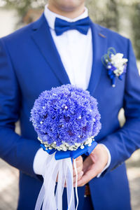 Midsection of groom holding bouquet