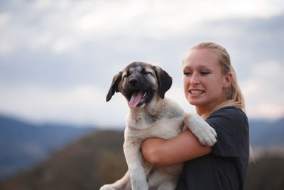 Young woman carrying dog while standing against sky