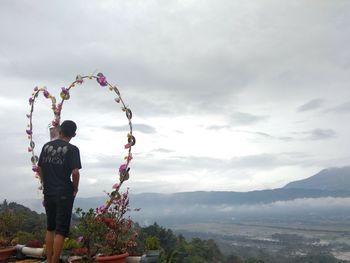 Rear view of man standing on mountain against sky