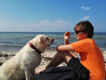 Side view of boy with labrador retriever on shore at beach