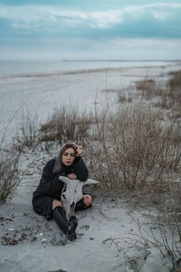 Woman sitting on shore at beach against sky