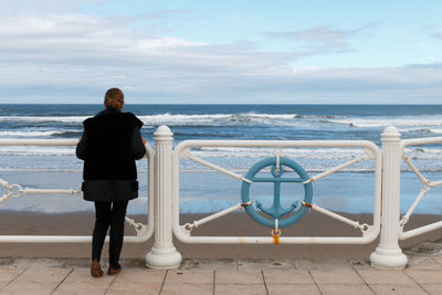 Rear view of man standing on railing against sea