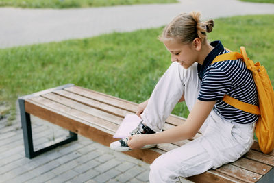 A cute teenage girl is sitting on a bench and tying her shoelaces