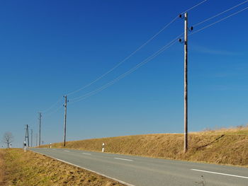 Electricity pylons on field against clear blue sky