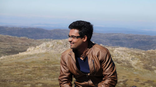 Young man wearing sunglasses standing on mountain against sky