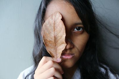 Close-up portrait of young woman holding dry leaf