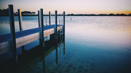 Wooden post on pier by sea against sky during sunset