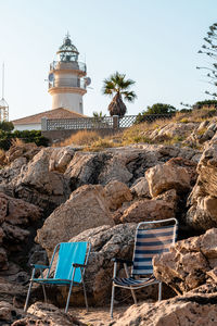 Sunrise over the lighthouse of cullera, with two beach chairs next to a rocks, in valencia spain