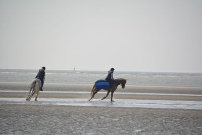 Women riding horses at beach against sky