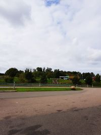 Road by trees on field against sky