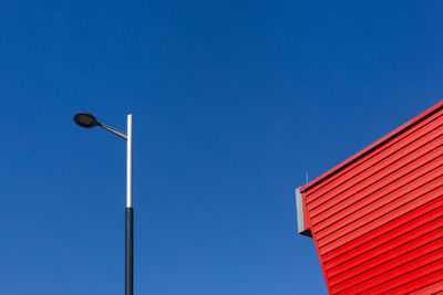 Low angle view of street light by building against clear blue sky