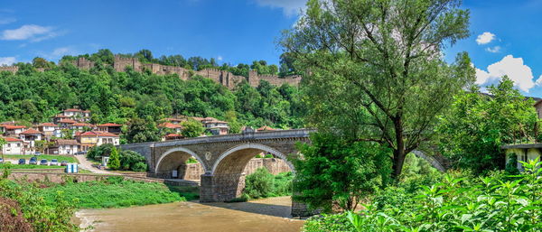 Arch bridge amidst trees and buildings against sky