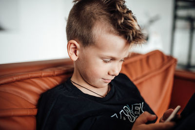 Smiling boy using smart phone while sitting on sofa at home