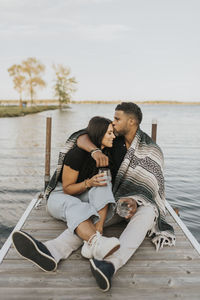 Man kissing woman while sitting on pier against lake