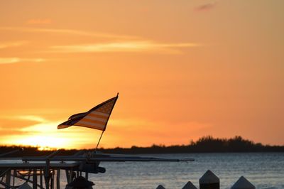 Silhouette flag on beach against orange sky