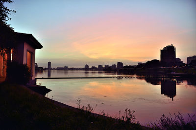 Buildings by river against sky during sunset