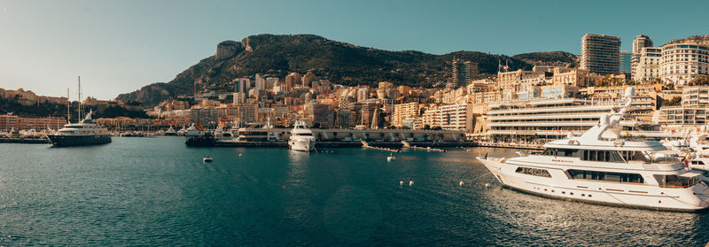 Sailboats moored on sea by buildings against clear sky