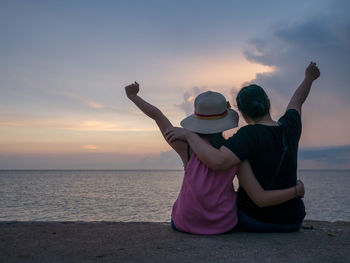 Friends sitting at beach against sky during sunset