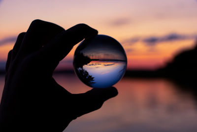 Close-up of hand holding glass against sky during sunset