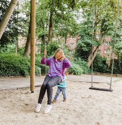 Granddaughter pushing grandmother sitting on swing in playground