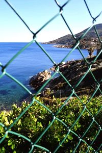 Close-up of sea seen through chainlink fence against clear sky