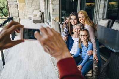 Cropped hands of senior man photographing happy family through smart phone on porch