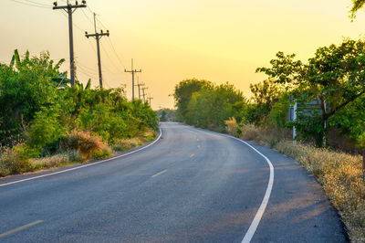 Empty road by trees against sky