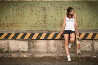 Young woman looking away while standing against wall