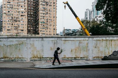 Side view of woman walking on sidewalk against wall in city