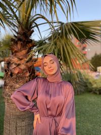 Portrait of young woman standing against palm tree