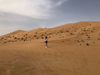 Woman standing on sand dune in desert against sky