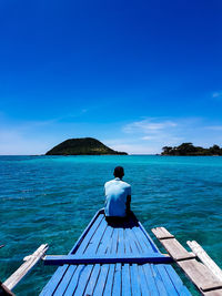 Rear view of man looking at sea against blue sky