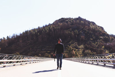 Full length of man walking on bridge against mountain during sunny day