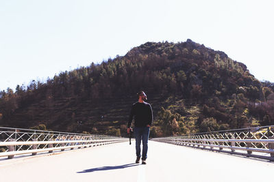 Rear view of man standing on mountain against clear sky