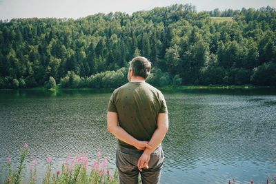 Rear view of man looking at lake against trees