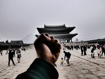 Cropped image of man fist by gyeongbokgung against clear sky