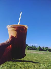 Cropped image of person holding drink against blue sky