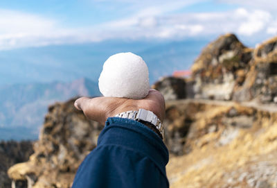 Midsection of person holding rock in sea against sky